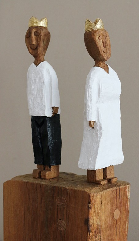 Zwei Holzfiguren mit Kronen, eine in weißem Kleid, eine mit schwarzer Hose.