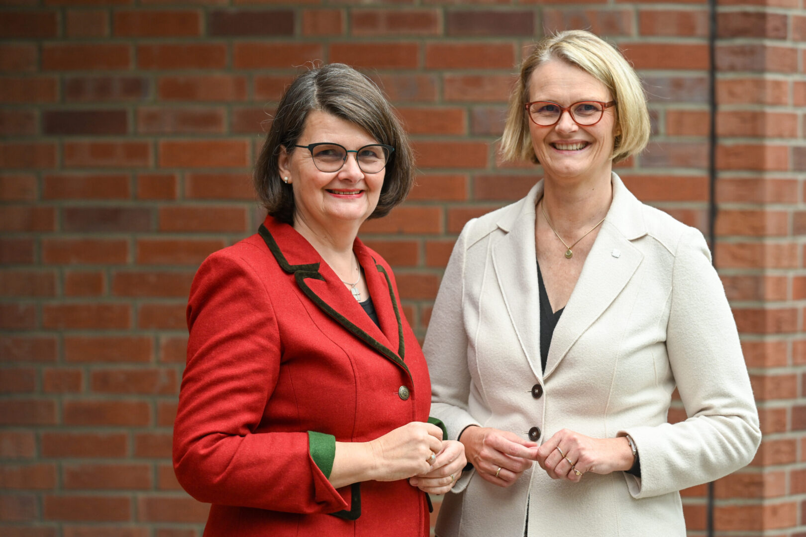 Die ehemalige KDFB-Präsidentin Dr. Maria Flachsbarth (l.) steht neben der neuen KDFB-Präsidentin Anja Karliczek vor einem Backsteingebäude. Beide lächeln.
