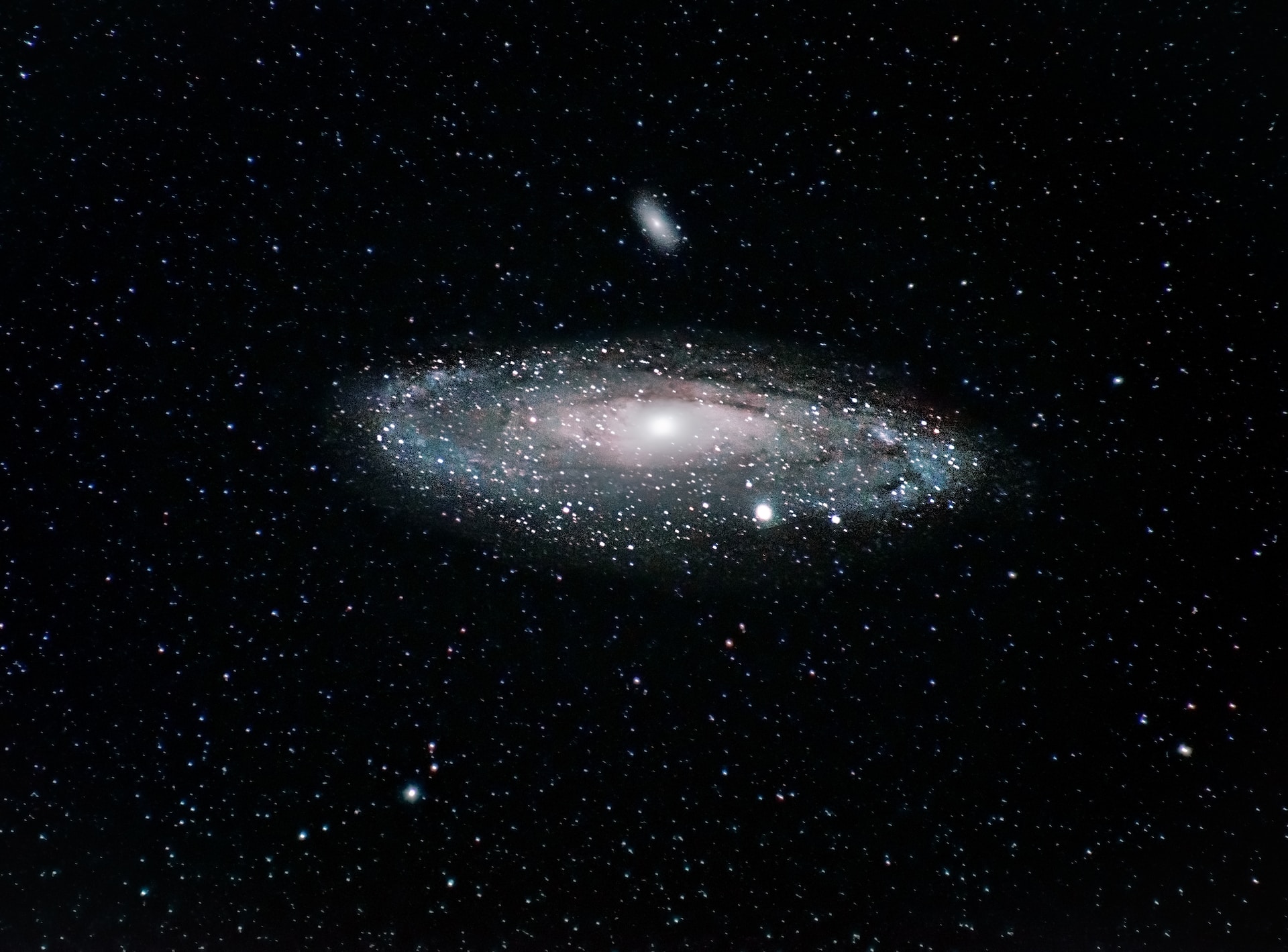 Zu sehen ist ein nächtliches Weltraumbild, mittig ein Andromedanebel.