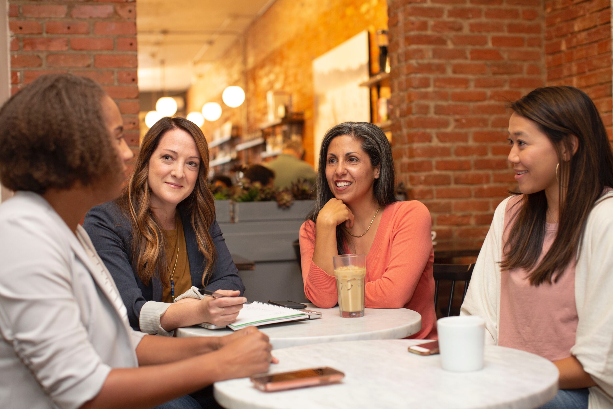 Vier Frauen in Businesskleidung sitzen an einem Tisch, trinken Kaffee und unterhalten sich.